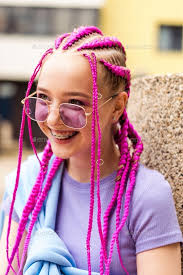 Smiling caucasian teenage girl with pink braids and with braces on her  teeth on a street background.